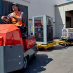 Taylor-Dunn C-426 Tow Tractor utility vehicle hauling industrial carts outdoors.