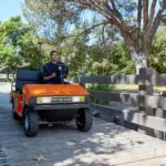 Taylor-Dunn R-380 Personnel Carrier Utility Vehicle crossing wooden bridge outdoors.