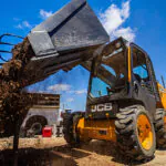 JCB 215 Skid Steer dumping dirt into wheelbarrow.