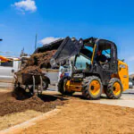 JCB 215 Skid Steer dumping dirt into wheelbarrow on construction jobsite.