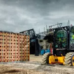 JCB 3TS-8W skid steer transporting pallet of bricks.