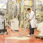 Operator using Nilfisk S3 industrial vacuum to clean dry spill on floor.