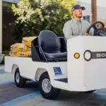 Taylor-Dunn Bigfoot S Burden Carrier driving outdoors transporting materials.