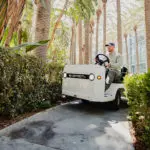 Taylor-Dunn Bigfoot S burden carrier driving on outdoor sidewalk.