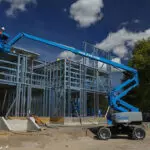 Genie Z-60 DC Articulating Boom Lift lifting construction worker towards top of building frame.