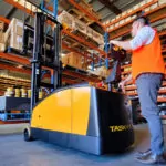 Operator using TASK Cobra legless stacker to grab pallet of boxes off warehouse shelf.
