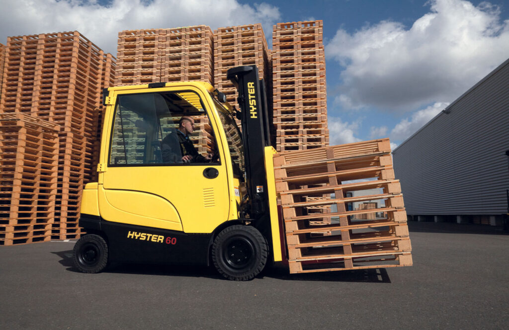 Hyster J60XN electric forklift transporting a stack of empty pallets in an outdoor lot.
