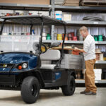 Man loading tools and materials into Cushman Hauler 1200 Utility Vehicle cargo bed.