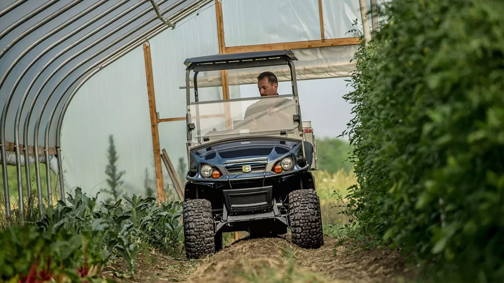 Cushman Hauler 1200X utility vehicle driving through greenhouse with rough terrain.