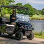 Cushman Hauler utility vehicle driving on path near pond.