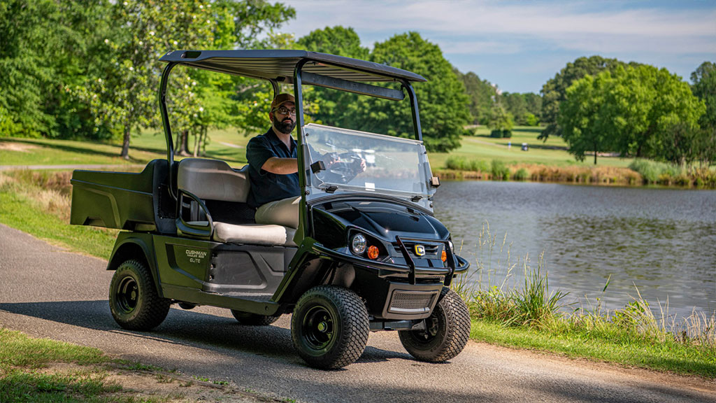 Cushman Hauler utility vehicle driving on path near pond.