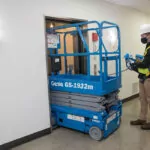 Genie GS-1932m scissor lift lowered, driving through doorway.