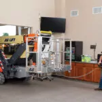 JLG X1000AJ compact crawler boom lift driving through doorway.