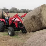 Mahindra 4550 4WD Tractor with special attachments transporting 2 large hay bales.