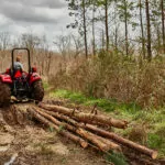 Mahindra 5100 Series Tractor hauling logs through forest path.