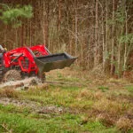 Mahindra 5100 Series Tractor with bucket attachment driving through muddy, flooded field.