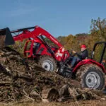 Mahindra 5145 4WD Tractor with bucket loader attachment climbing up a hill of logs and sticks.