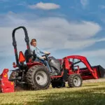 Mahindra MAX 26 XLT HST tractor driving in field cutting grass with lawn cutter attachment.