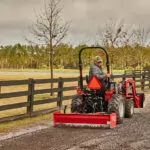 Mahindra MAX 26 XLT HST driving on gravel pathway with attachment.