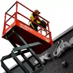 Skyjack SJ3219 E electric scissor lift raising worker to top of Skyjack building.