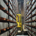 Combilift COMBI-AGT autonomous guided forklift truck maneuvering with a wide load through narrow aisles.