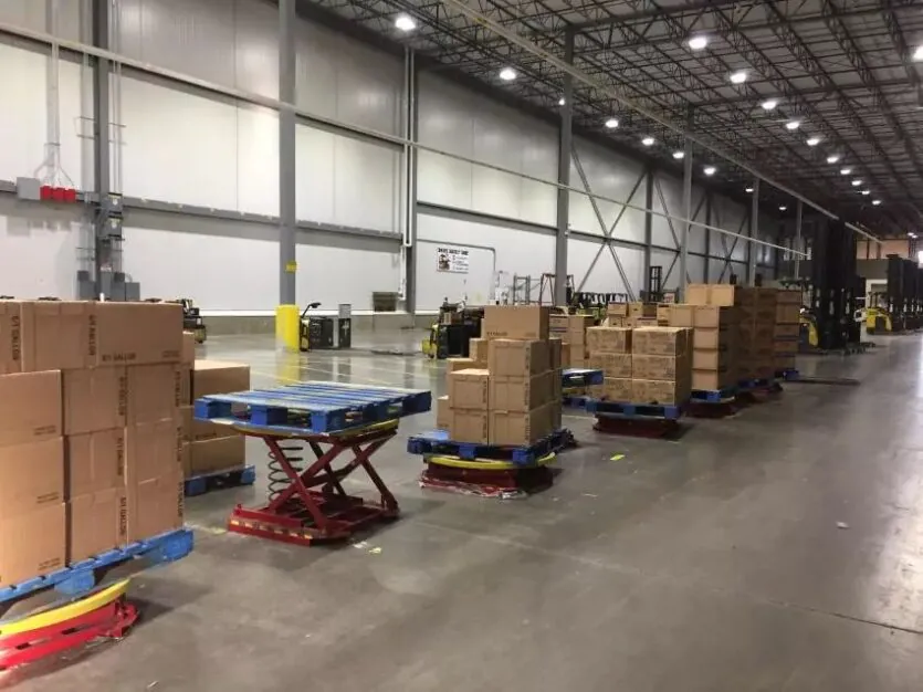 Lift tables holding pallets of materials along warehouse wall.