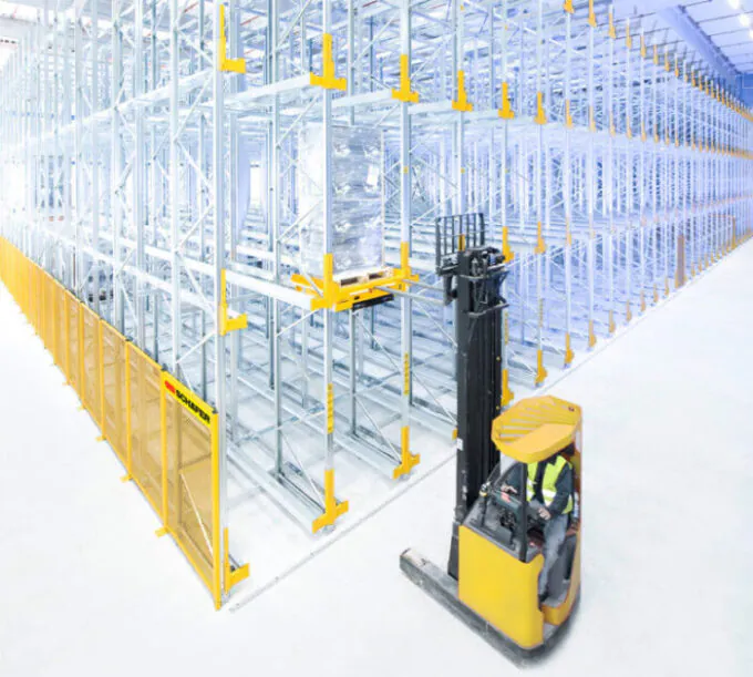 Narrow aisle forklift lifting pallet onto racking SSI Schaefer pallet shuttle in warehouse.