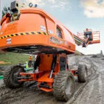 JLG 670SJ boom lift driving on rough dirt terrain.