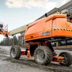 JLG 670SJ telescopic self-leveling boom lift driving on dirt road.