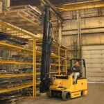 Drexel SL80AC electric forklift lifting pallet onto warehouse shelf.