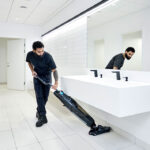 Worker cleaning bathroom floor with Dryft micro scrubber.