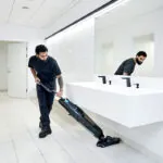 Worker cleaning bathroom floor with Dryft micro scrubber.