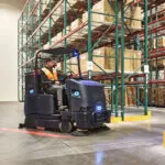 Nilfisk Advance CS7500 Sweeper Scrubber turning into warehouse aisle.