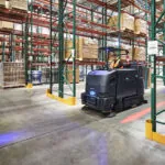 Nilfisk Advance CS7500 Sweeper Scrubber exiting warehouse aisle.