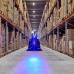 Nilfisk SW3000 rider sweeper cleaning floors in warehouse aisle.