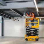 JCB S1932E electric scissor lift in empty warehouse room.