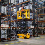 JCB S1932E scissor lift raised in warehouse aisle.