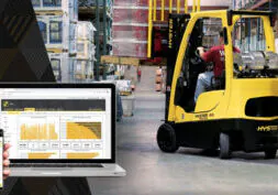 Hyster forklift in warehouse, with telematics tracking data visible on nearby computer and phone.